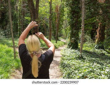 Blonde Woman Taking A Picture In A Forest.