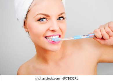 Blonde Woman With A Towel On Her Head Brushing Her Teeth