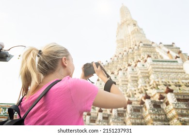 Blonde Woman Traveler Taking Travel Photo Of Wat Arun Or Temple Of Dawn In Bangkok, Thailand