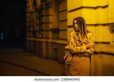 Blonde woman in trench coat feeling cold and worried while walking on a streets of a big city during night. Female holding her hands crossed and looking away not feeling safe to be all alone. - Powered by Shutterstock