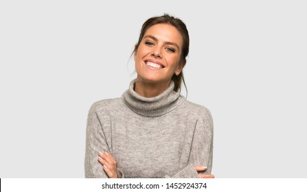 Blonde woman with turtleneck keeping the arms crossed in frontal position over isolated grey background