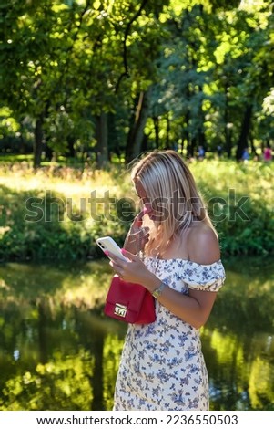 Blonde woman using mobile phone for message summer park, walking outdoors, text messaging. Concept vacation and leisure activity lifestyles. Outdoor of adult female model outside. Copy text space