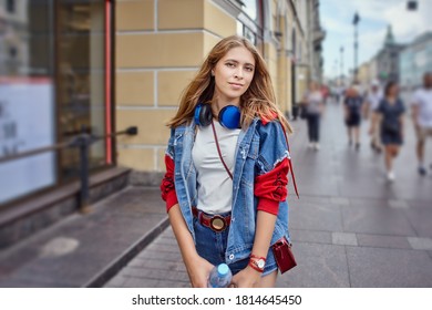 Blonde woman is walking on the crowded street. Caucasian attractive girl 20 years old in shorts in the city center.
