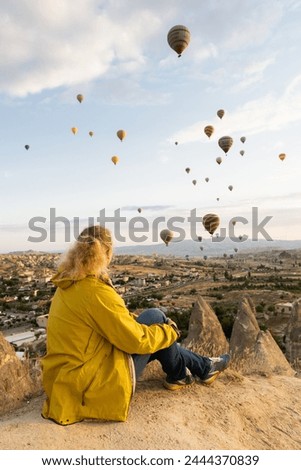 Blonde woman watching balloons flying over Cappadocia fairy chimney valley at sunrise in Goreme, Turkey