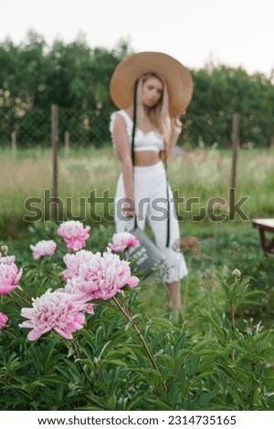 A blonde woman is watering flowers in the garden in the courtyard of a village house. The concept of a summer cottage