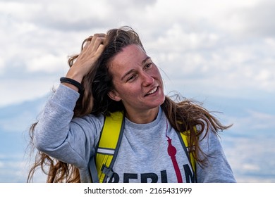 Blonde Woman With Wavy Hair, Sitting On A Rock While Resting On A Mountain Hiking Trail.