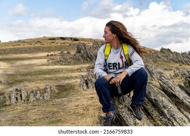 Blonde Woman With Wavy Hair, Sitting On A Rock While Resting On A Mountain Hiking Trail.