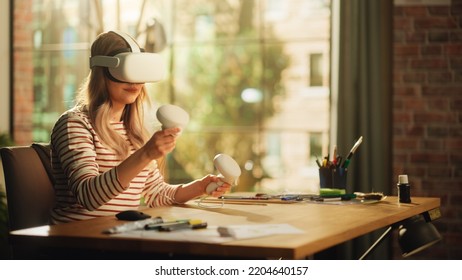 Blonde Woman Wearing 3D VR Headset And Using Modern Controllers in Loft Apartment Living Room. Female Designer Working in Futuristic Application. New Technologies and Augmented Reality Hologram. - Powered by Shutterstock