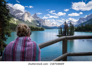 Blonde Woman Wearing A Pink Blanket, Enjoys The View Of Spirit Island On Maligne Lake In Alberta Canada