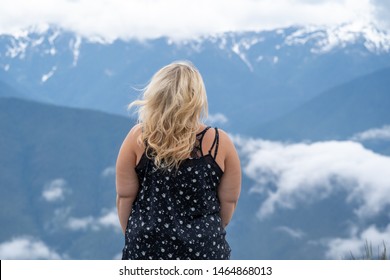 Blonde woman wearing tank top poses for a portrait with the Cascade Mountains in background. Hair blowing in wind - Powered by Shutterstock