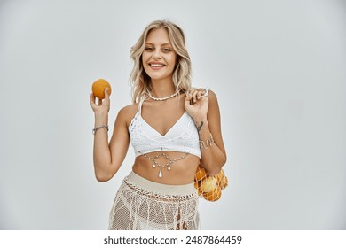 A blonde woman in white beachwear smiles while holding an orange, exuding summer vibes. - Powered by Shutterstock