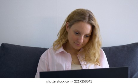 A Blonde Woman Works At A Computer At Home, Remote Work And Training In A Simple Home Environment And Casual Clothes. Beautiful Woman Working On A Project At Home With A Laptop.