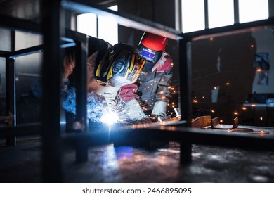 Blonde woman works as a welder in workshop, operating welding machine, wearing protective clothing and a welding mask. Two welders helpign each other. - Powered by Shutterstock