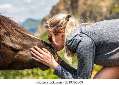 Blonde young female animal lover kissing a wild horse on its nose - Powered by Shutterstock