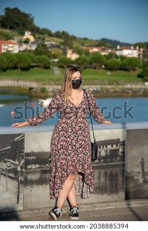 Blonde Young Girl with flowered dress and a black face mask with the River at the back on a sunny clear day