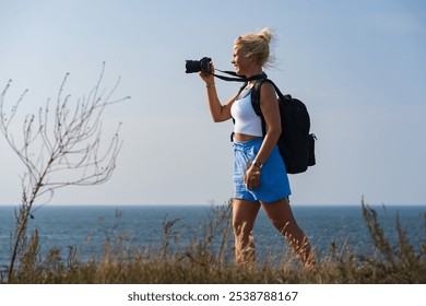 Blonde young girl landscape photographer takes a picture on the seashore on a summer day, photo view from the side. - Powered by Shutterstock