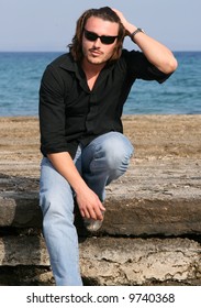 Blonde young man with sunglasses sitting on a rock