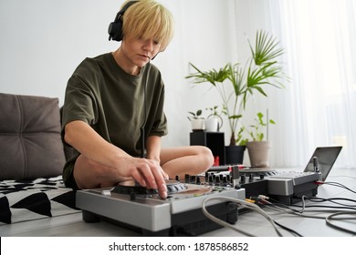Blonde young short haired woman wearing headphones push the button at the dj console or controller. Top view of female producer at home studio with modern electronic instruments