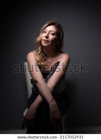Blonde young woman over gray wall background. Dramatic lighting and portrait at studio photoshoot.
