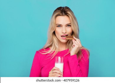 Blonde Young Woman In Pink Blouse Eating Chocolate Biscuit With Milk On Blue Background