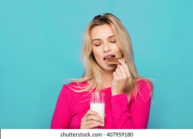 Blonde Young Woman In Pink Blouse Eating Chocolate Biscuit With Milk On Blue Background