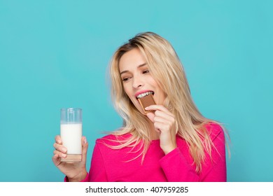 Blonde Young Woman In Pink Blouse Eating Chocolate Biscuit With Milk On Blue Background