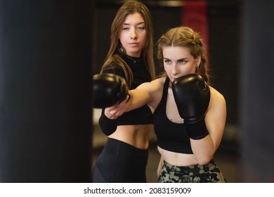 The blonde young woman, under the guidance of a trainer, performs blows on a punching bag. Women's fitness boxing workout in the gym.  - Powered by Shutterstock