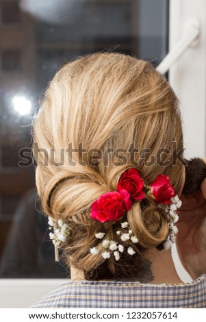 Blonde/light brown haired woman head wearing wedding bridal hairstyle with little red roses and white flowers in it.