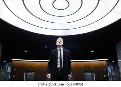 Blond-haired white collar worker posing for photography while standing in office lobby with creative design and looking upwards, portrait shot