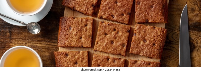 Blondie Brownie Dessert Bar With Chocolate Chips, Overhead Flat Lay Panorama With Tea On A Dark Rustic Wooden Background