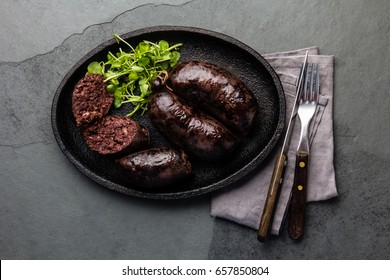 Blood bloody sausages on black cast iron plate with watercress salad. Gray slate background. Traditional chilean bloody sausage - prieta
