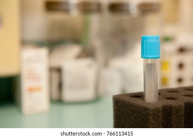 A Blood Collection Tube With Blue Cap Prominently Placed In A Foam Holder With Other Medical Supplies In The Background.  