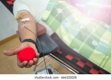 Blood Donor At Donation With A Bouncy Ball Holding In Hand. Close Up Right Arm Of Asian Man Giving Blood Donate In Hospital. Healthcare And Charity, Concept Image For World Blood Donor Day - June 14.