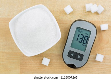 Blood Glucose Meter Device Showing High Blood Sugar Levels, Next To Bowl Of Sugar And Cubes On Wooden Background
