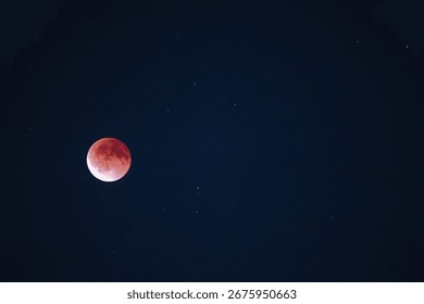 Blood moon during lunar eclipse glowing red in the night sky with visible stars around. High quality photo