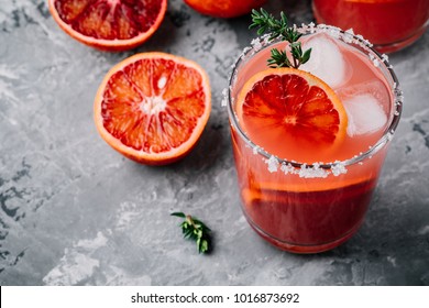 Blood Orange Margarita cocktail with ice and thyme on dark backgorund