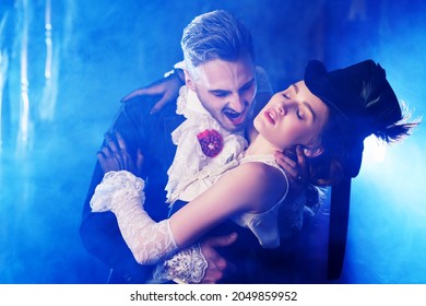 Bloodthirsty Male Vampire In Medieval Dress Is Biting A Beautiful Lady In An Old Castle. Halloween. Vampires.