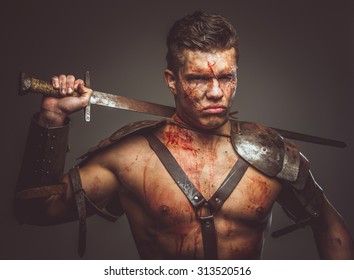 Bloody Gladiator In Armor Holding Sword On His Shoulder. Isolated On Grey Background.