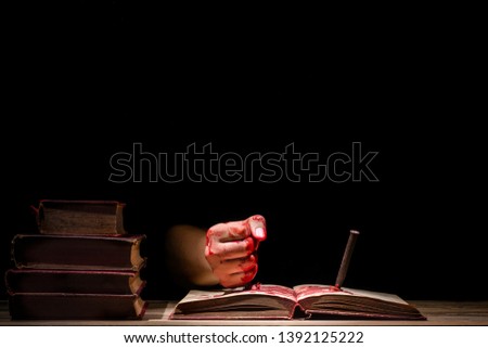 bloody hand stab an old book with pin or nail, horror concept