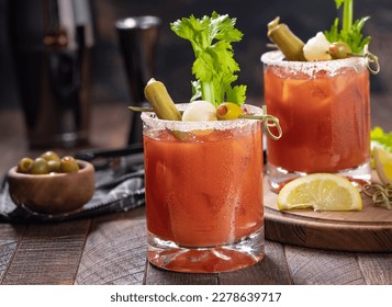 Bloody mary cocktail garnished with celery, okra, onion, olive and salt rim on a rustc wooden table