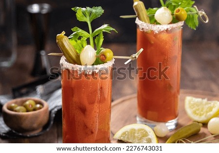 Bloody mary cocktail garnished with celery, okra, onion, olive and salt rim on a dark wooden background
