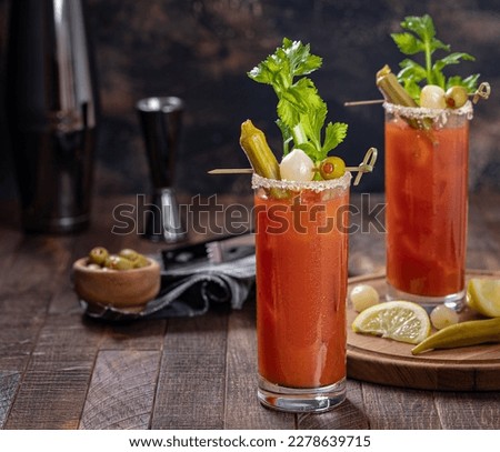 Bloody mary cocktail garnished with celery, okra, onion, olive and salt rim on a ddark wooden background