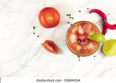 Bloody Mary Cocktail, Shot From Above On A White Marble Texture, With Red Hot Chili Peppers, Slices Of Lime, Tomatoes, And Copyspace