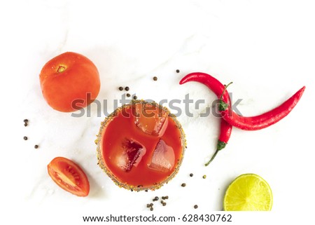 Bloody Mary cocktail, shot from above on a white marble texture, with red hot chili peppers, slices of lime, tomatoes, and copy space