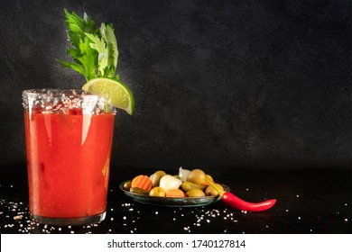 Bloody Mary cocktail with tomato juice, lime, and celery, wiuth pickles and a chili pepper, side view on a black background with copy space