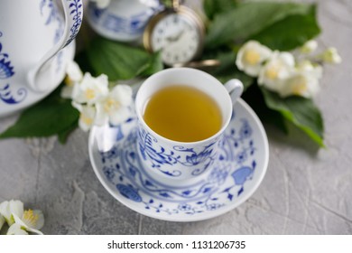 Blooming delicate jasmine flowers and a cup of green tea with a mechanical clock on the chain in the background.