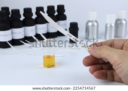 blotter paper is in a right hand with background essential oil and frangrance oil bottle for testing smell during blending process for choosing nice scent for scented candles and body perfume in lab