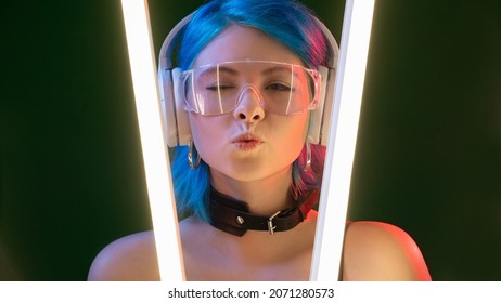 Blow kiss. Futuristic girl. DJ style. Pretty flirty winking woman in headphones pouts lips in LED lamp neon light on black background.