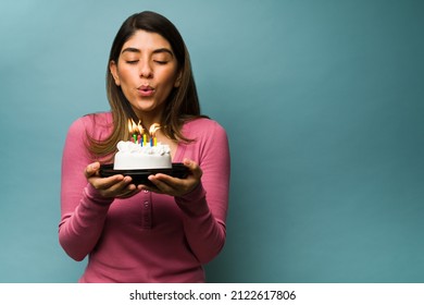 Blowing the birthday candles. Attractive young woman making a wish while holding a delicious cake next to copy space