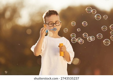 Blowing bubbles. Boy is having fun on the field under sunlight at daytime.